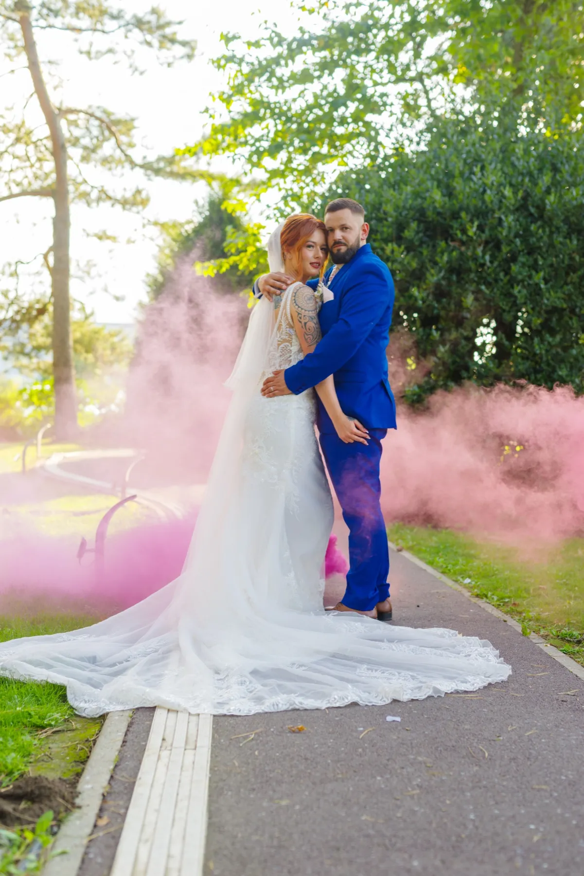 Les mariés enlacés sur une allée, dans un nuage de fumée rose