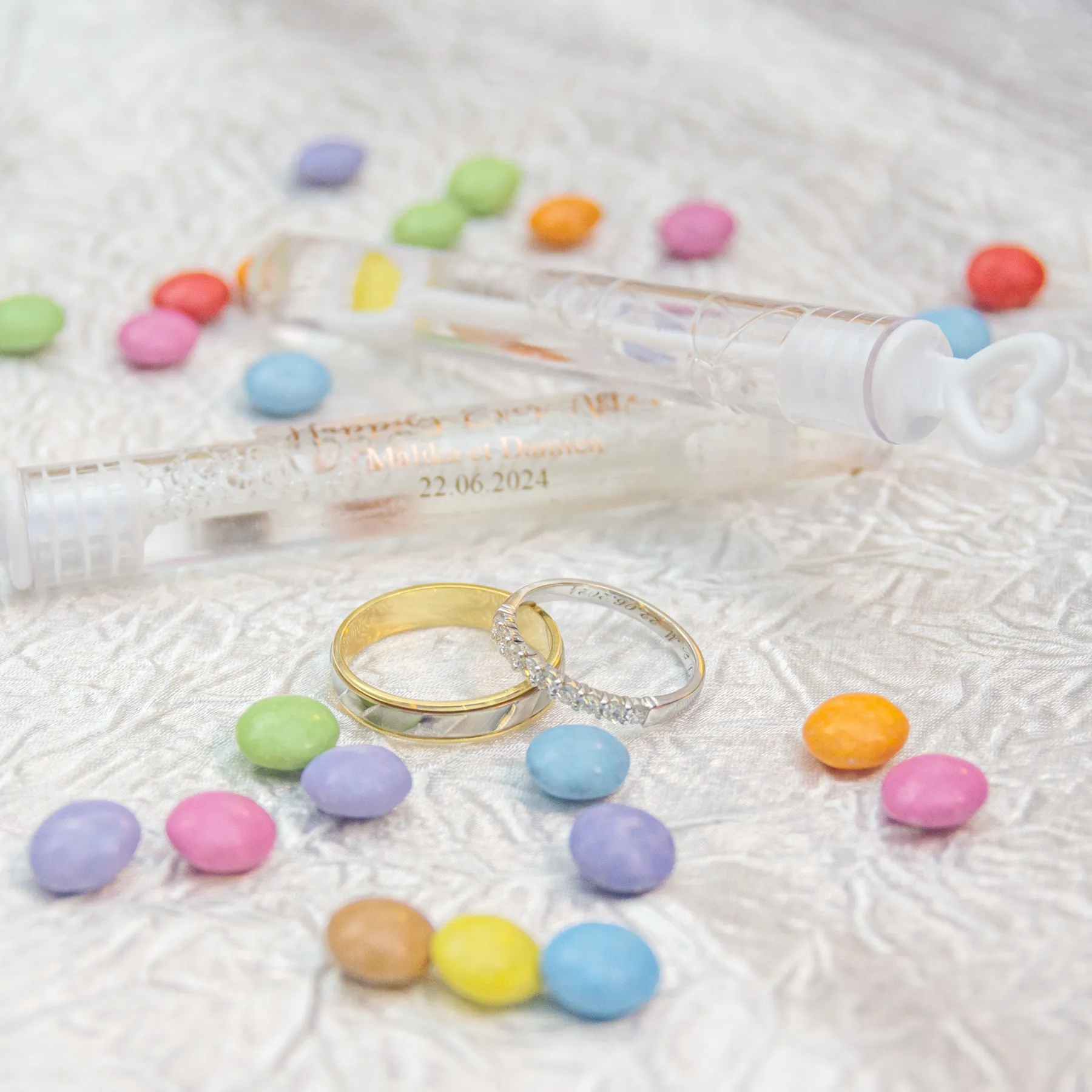 Les alliances sur un tissu blanc, parmi des bonbons de couleur et un tube à bulles