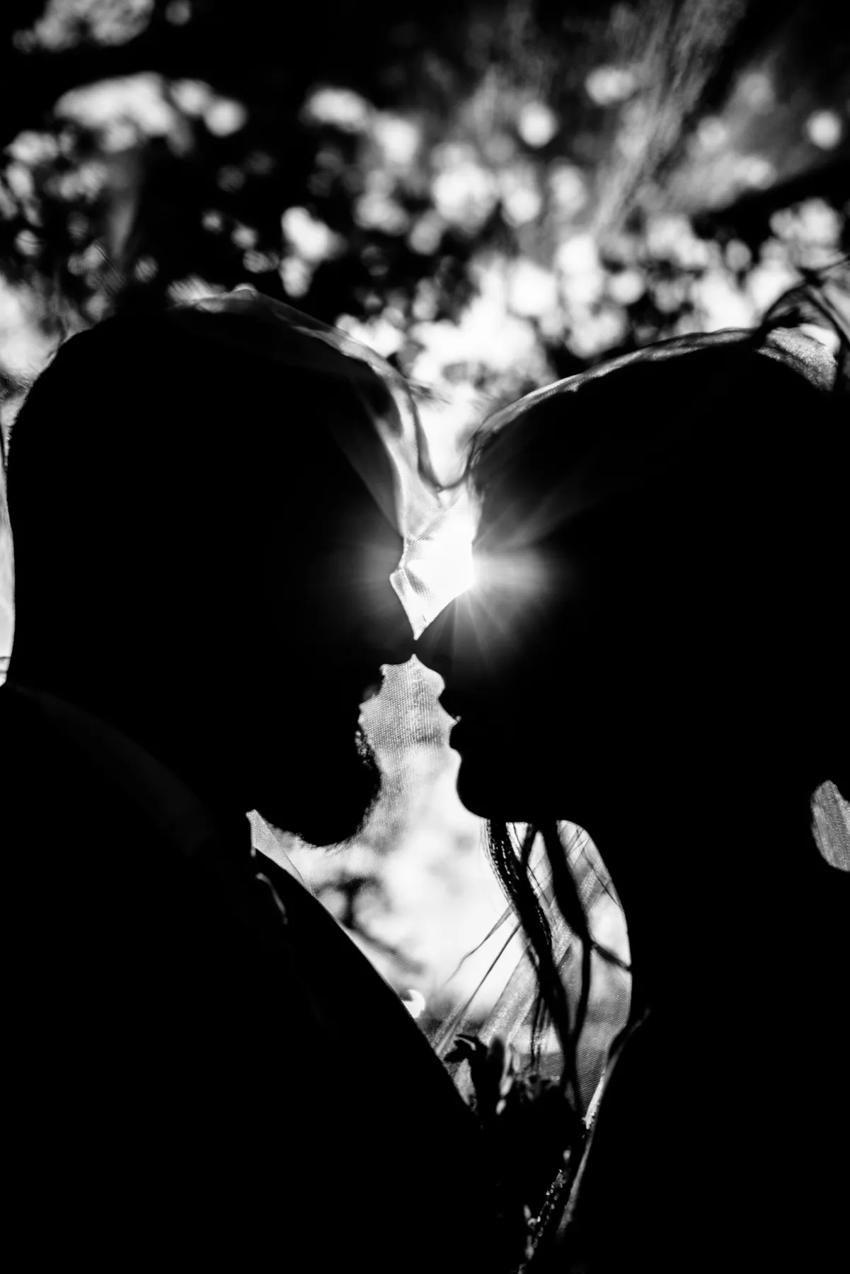En noir et blanc, les silhouettes des mariés face à face, le soleil entre leurs visages