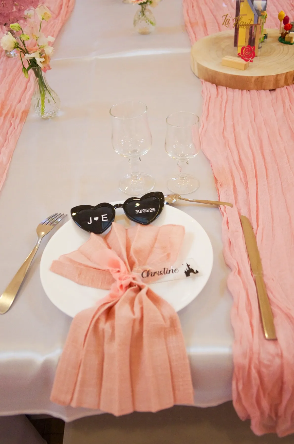 Une assiette dressée, serviette rose et lunettes en cœur marquées « J ♥ E »