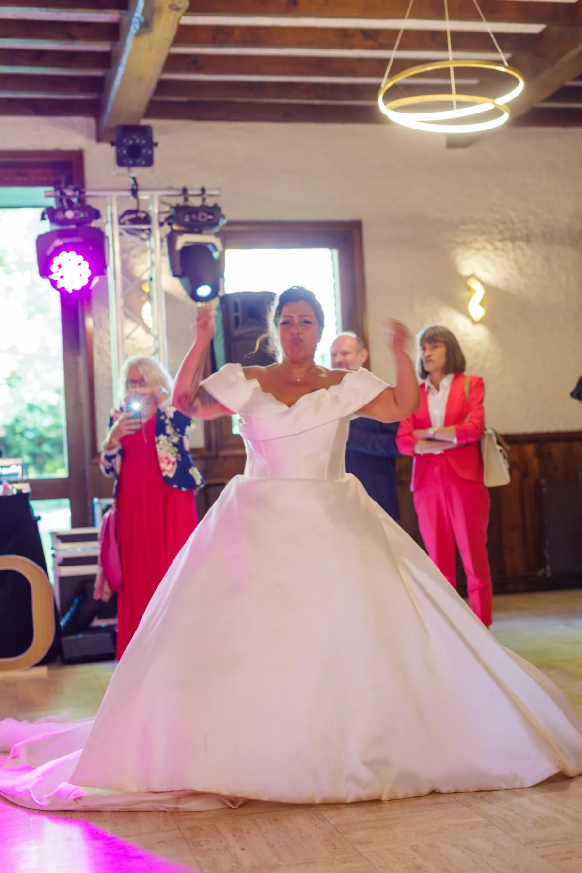 La mariée danse au milieu de la salle, les bras levés, dans sa grande robe blanche