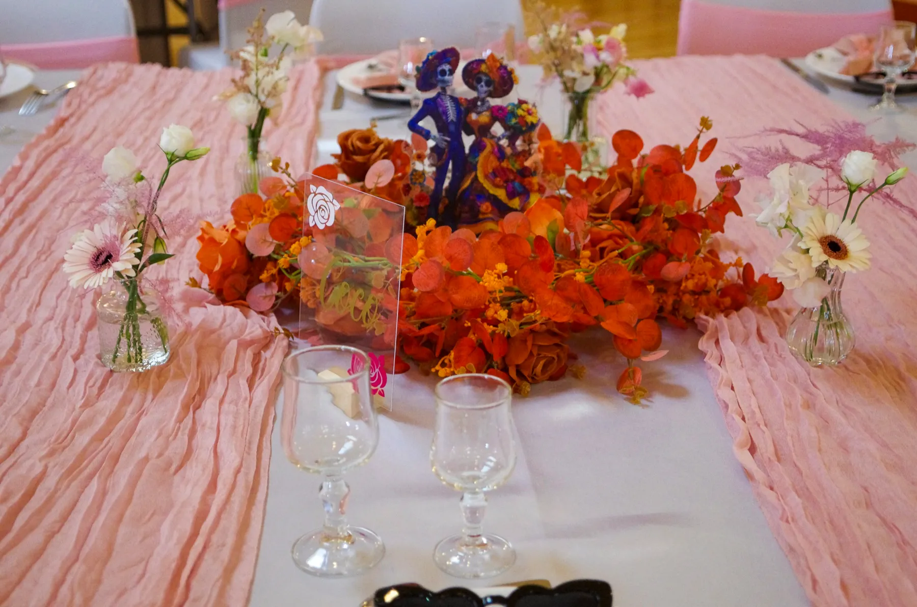 Un centre de table de fleurs orange et de figurines, sur un chemin de table rose