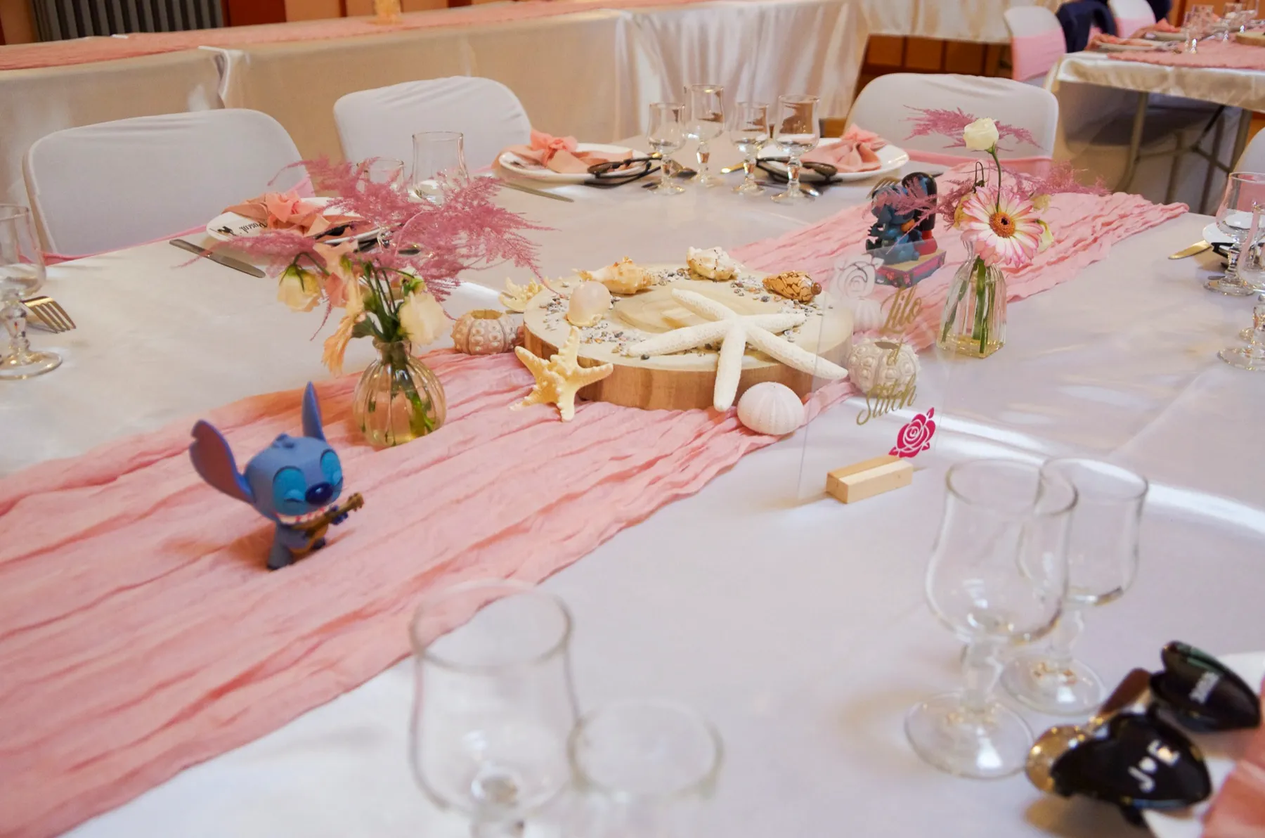 Une longue table dressée, chemin de table rose, coquillages et petite figurine bleue