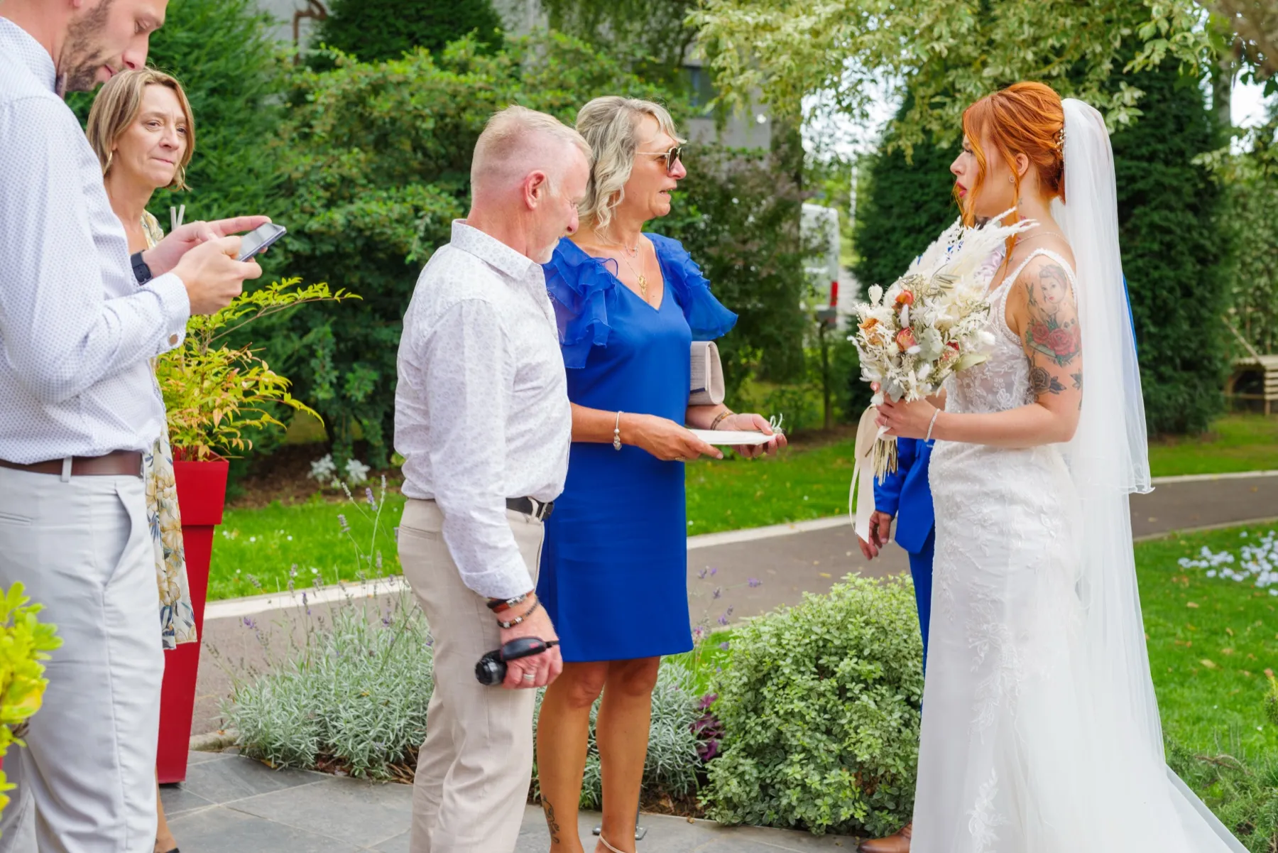La mariée, le bouquet à la main, échange quelques mots avec des invités dans le jardin