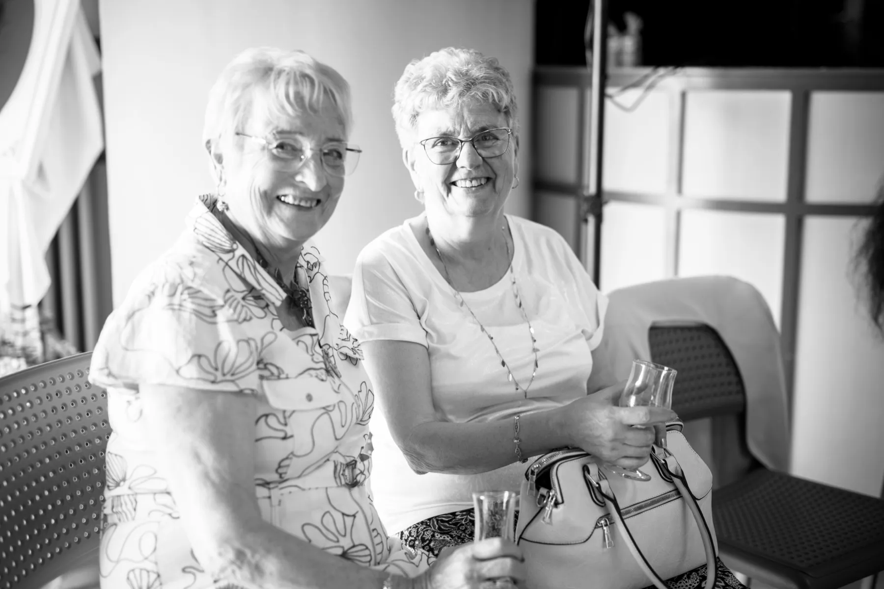 En noir et blanc, deux invitées assises sourient, une coupe à la main