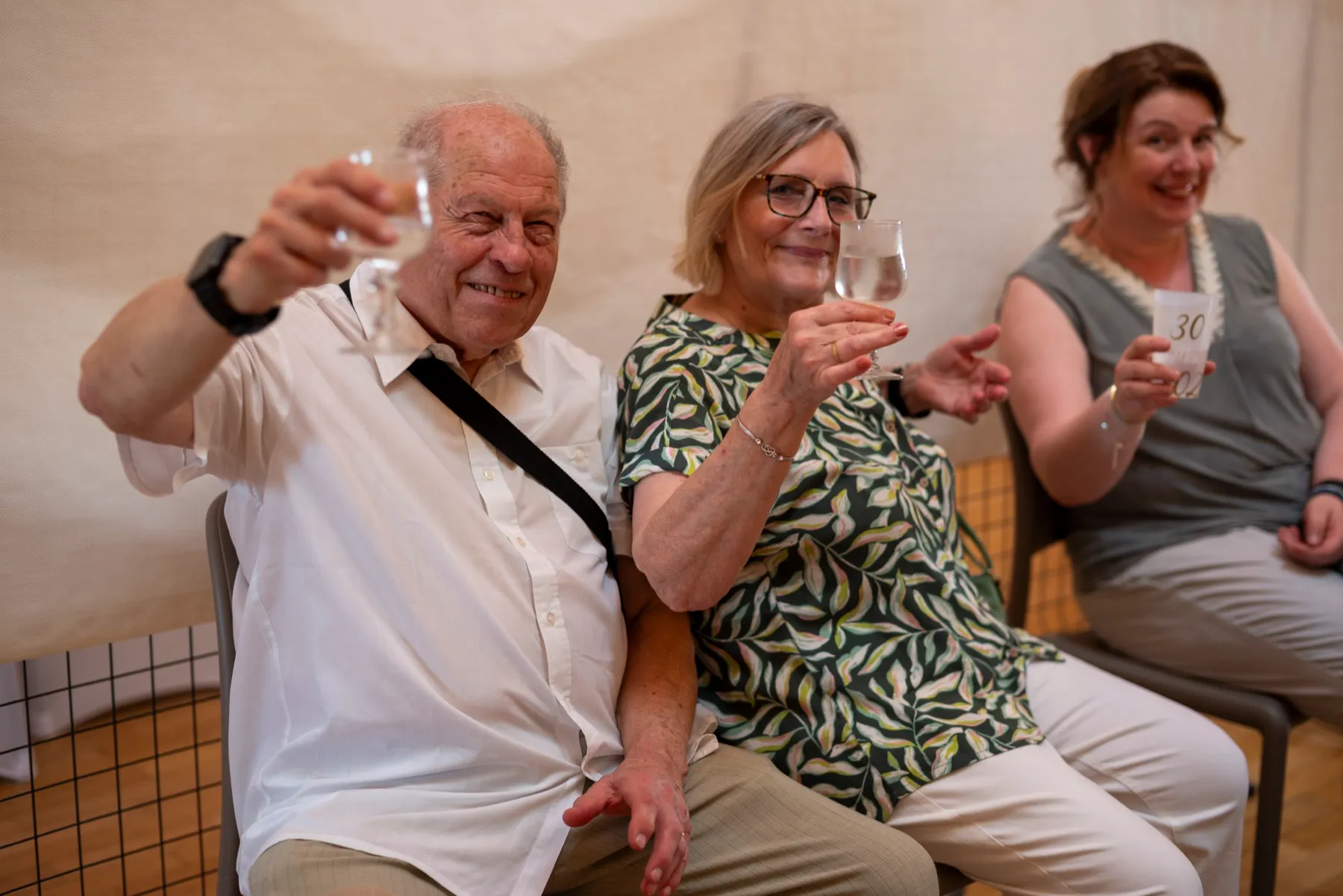 Trois invités assis lèvent leur verre en souriant