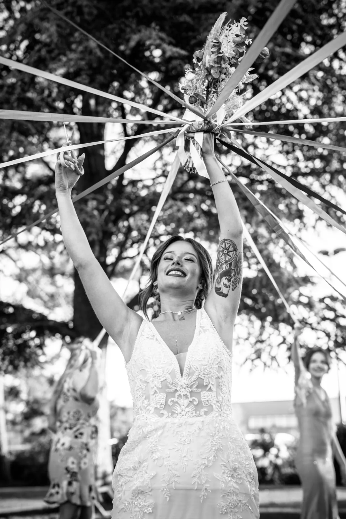 En noir et blanc, la mariée rit, les bras levés sous les rubans tendus