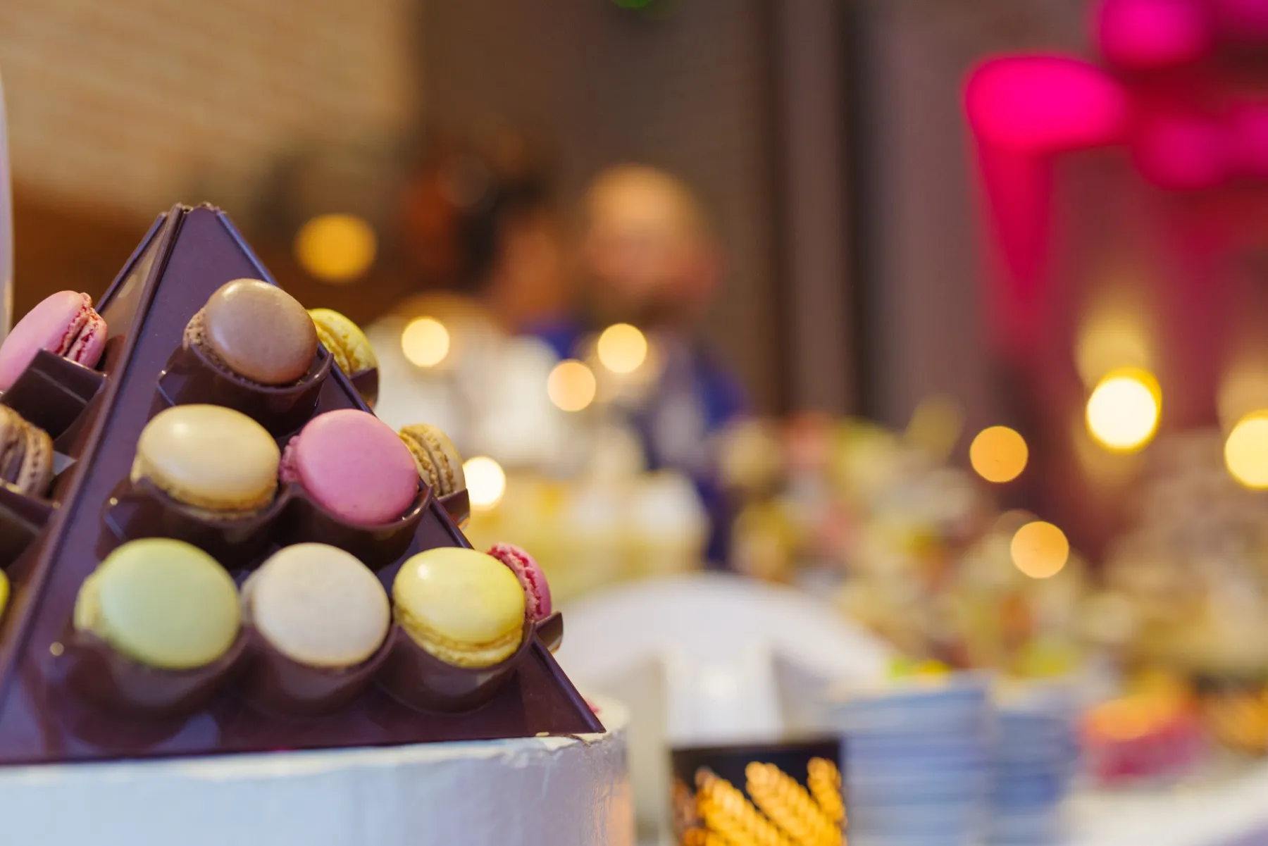 Gros plan sur une pyramide de macarons de toutes les couleurs, les lumières de la salle derrière