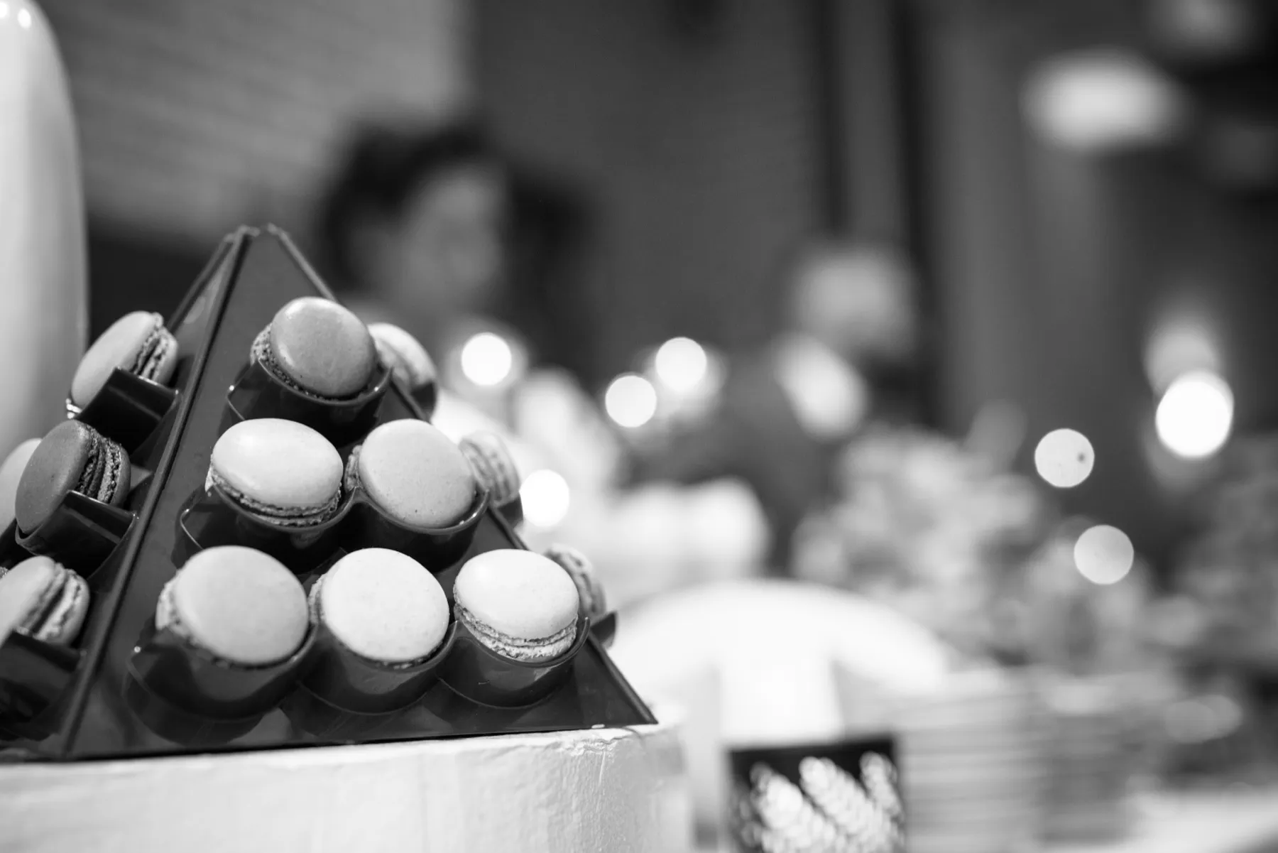 En noir et blanc, la pyramide de macarons devant les lumières floues de la salle