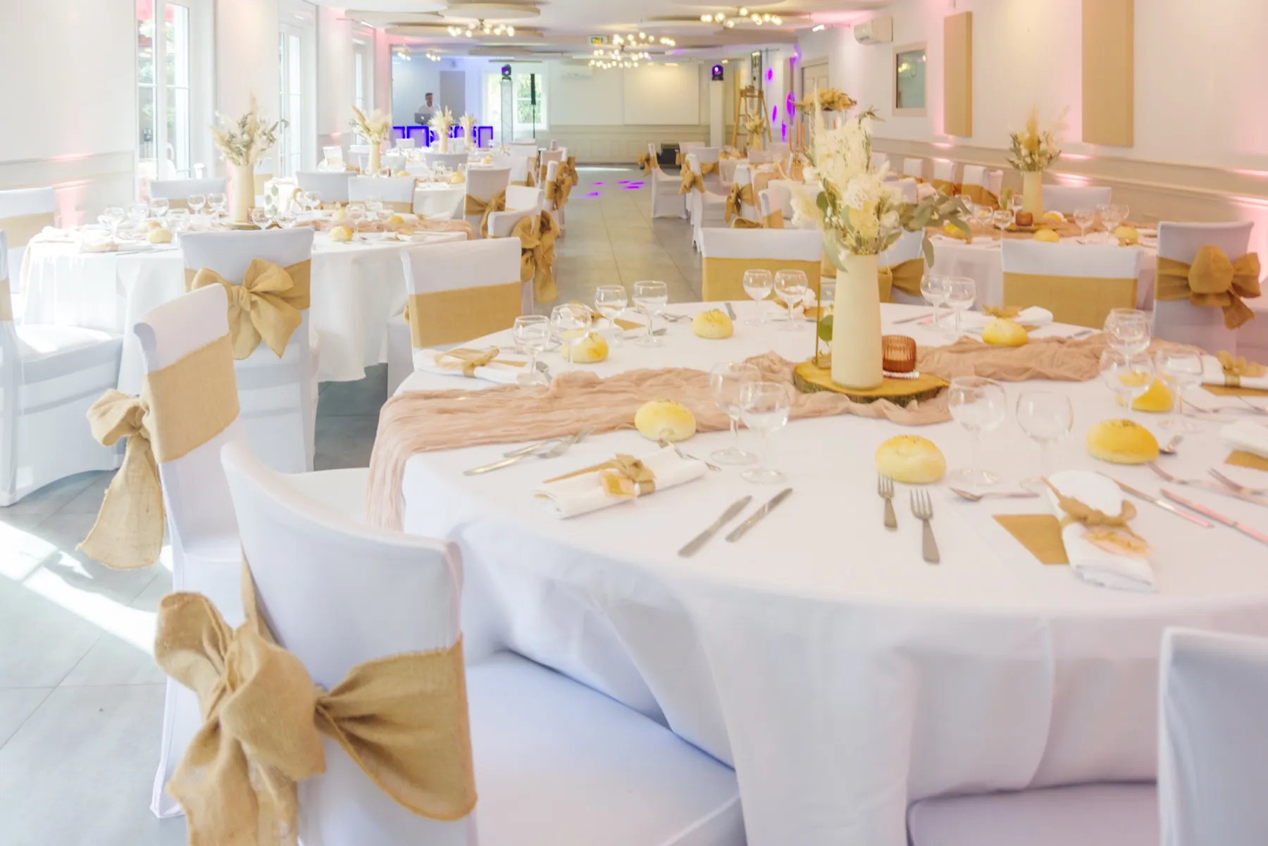 Tables rondes dressées en blanc, chemins de table rosés et nœuds en toile de jute