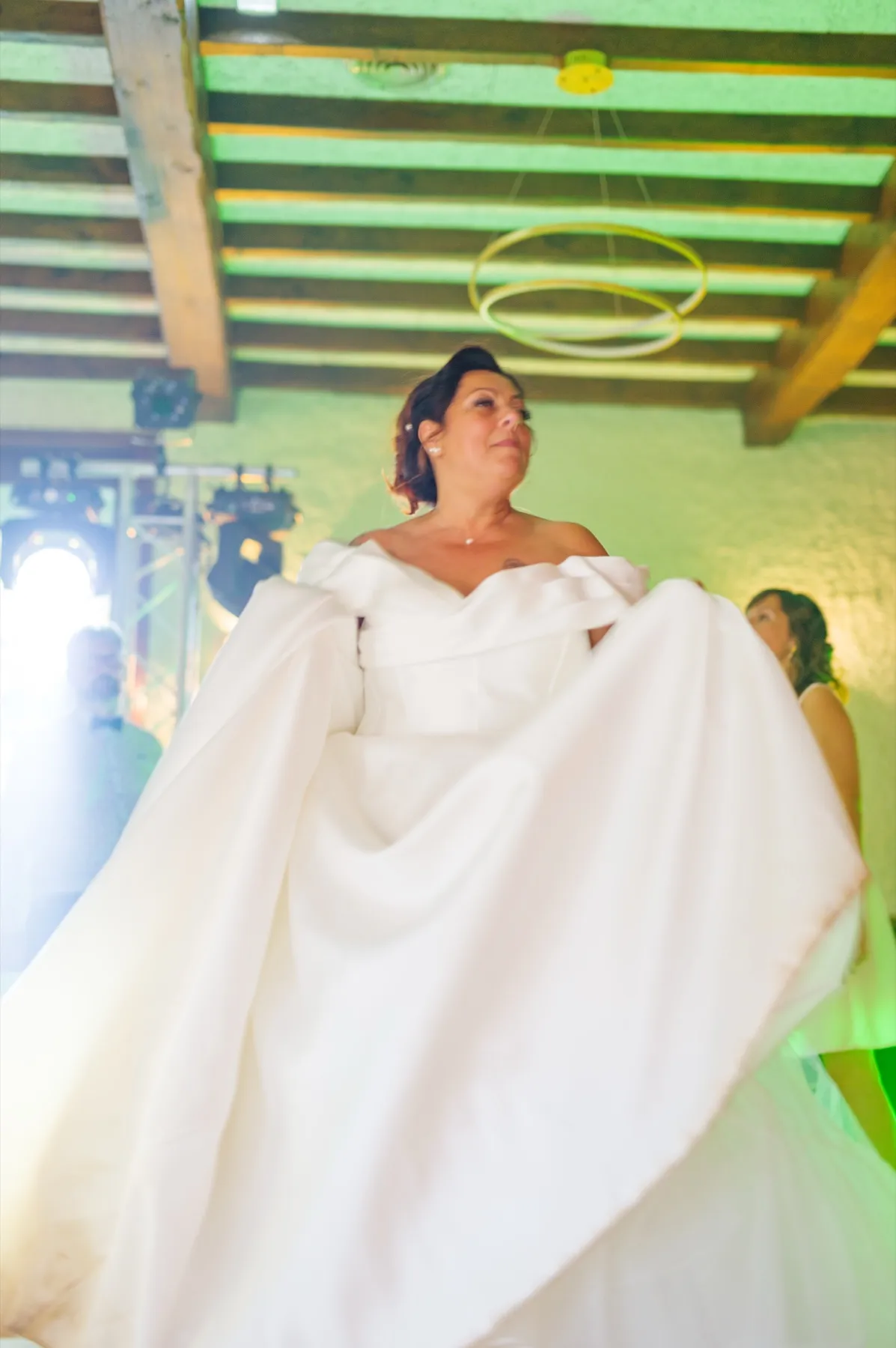 La mariée danse en tenant sa robe à pleines mains, sous les poutres de la salle