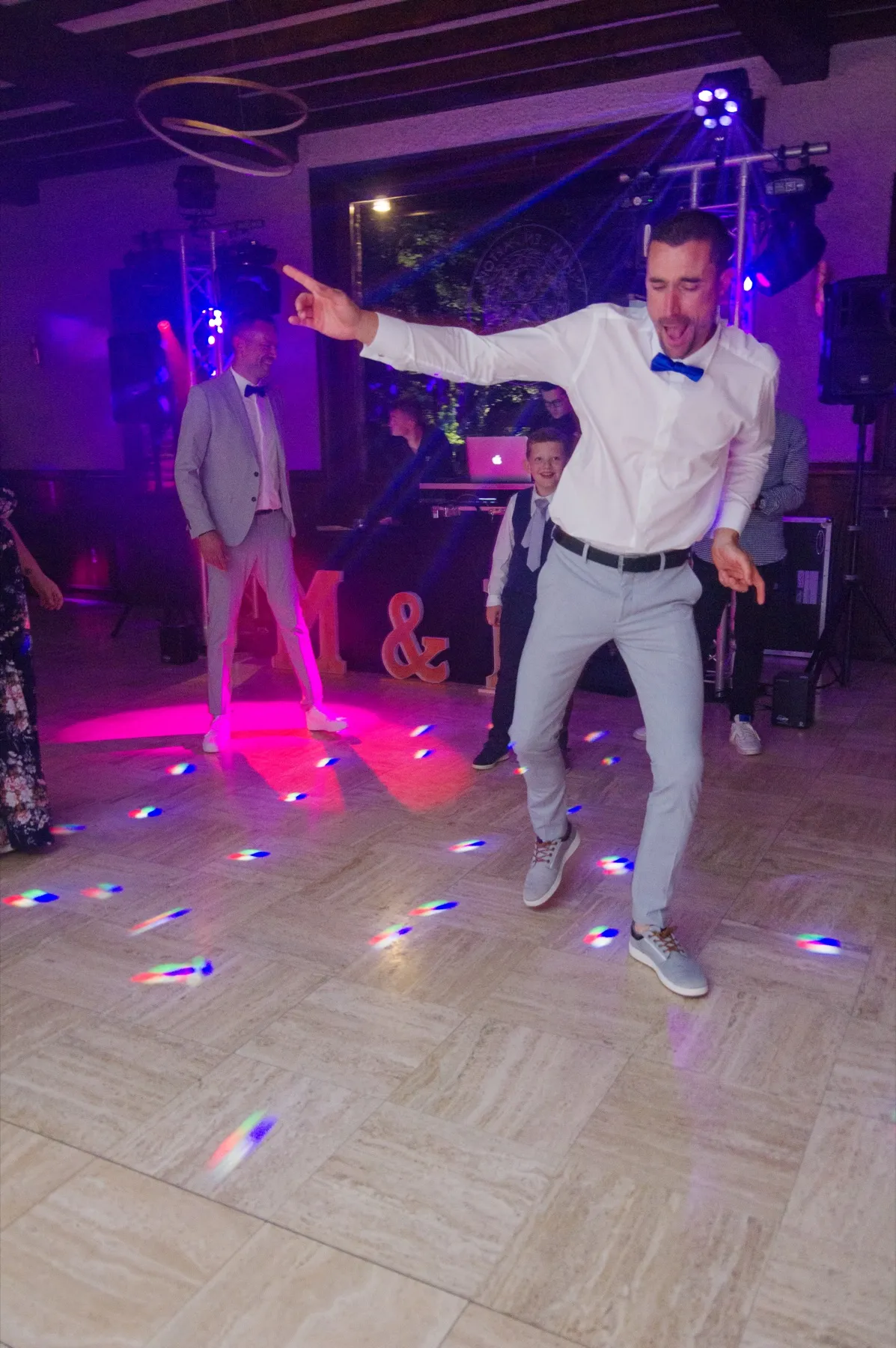 Un invité en chemise blanche et nœud papillon bleu danse au centre de la piste