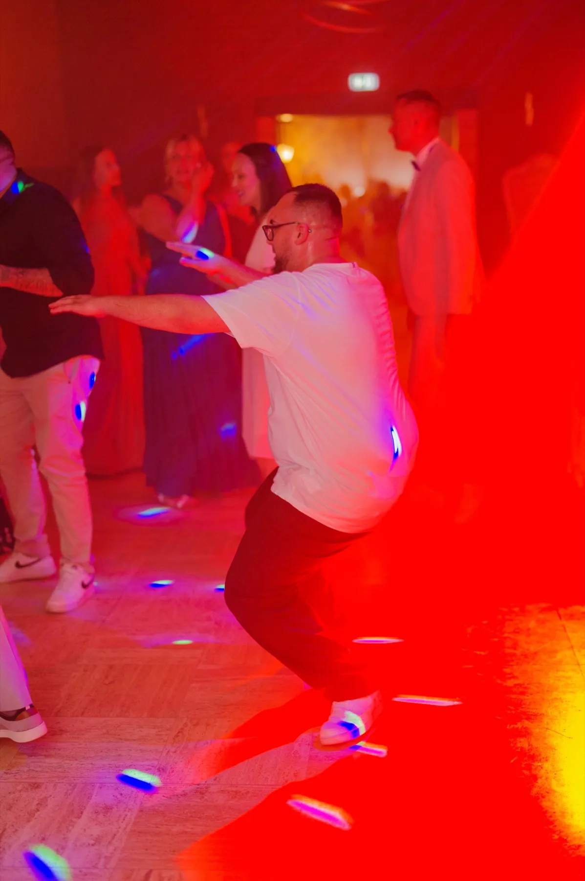 Dans une lumière rouge, un invité danse, les bras écartés, au milieu des autres