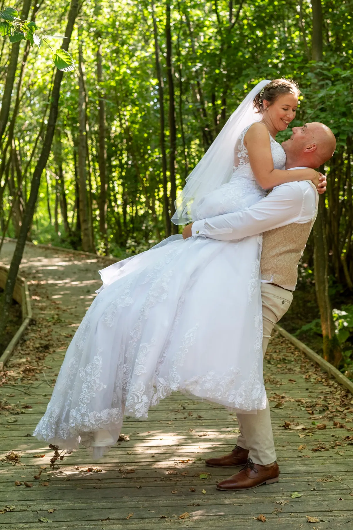 Le marié soulève la mariée sur une passerelle en bois, dans la forêt ensoleillée