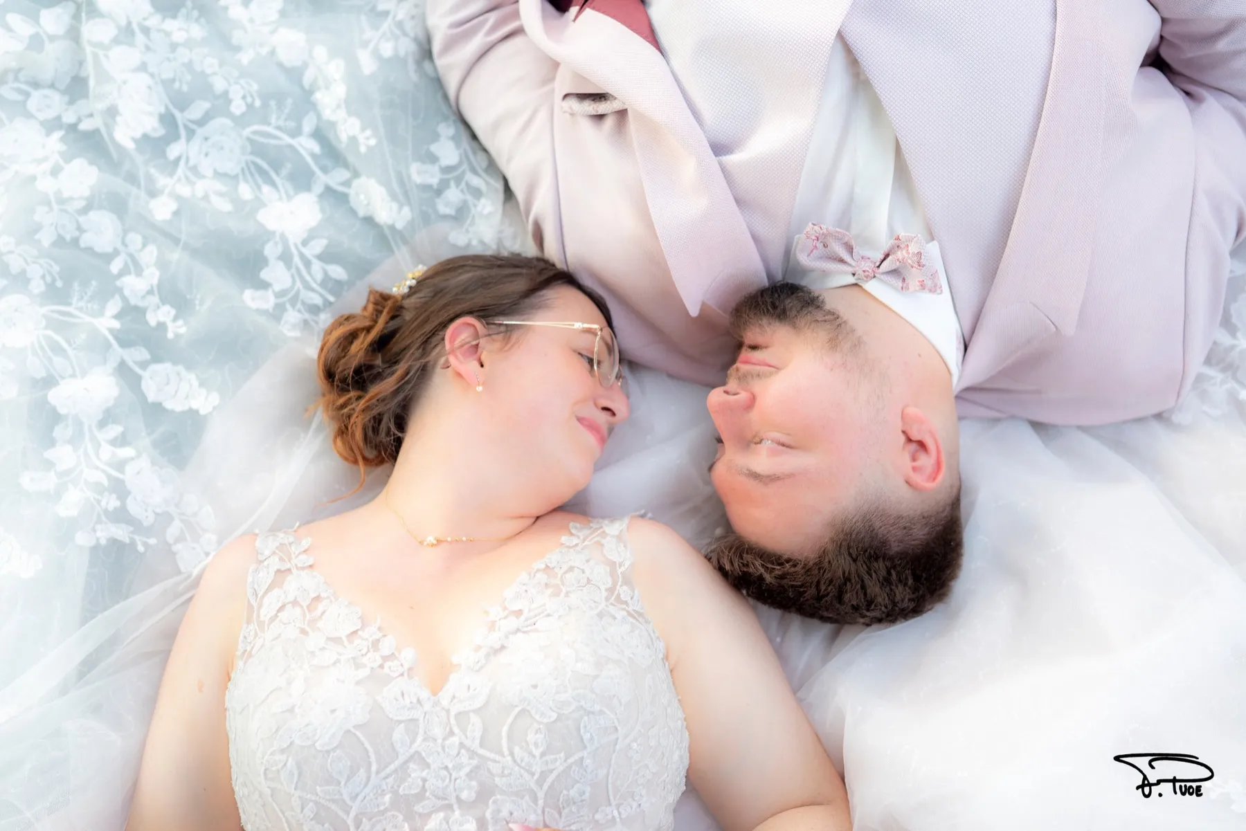 Les mariés allongés tête-bêche sur la robe, se regardant en souriant