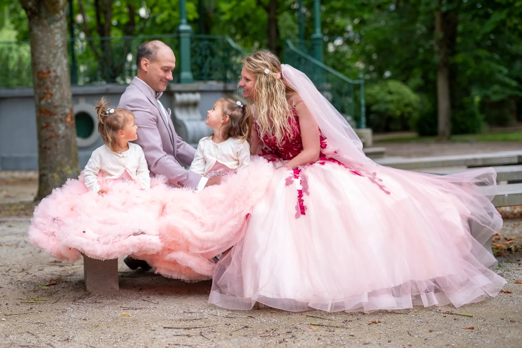 Les mariés assis sur un banc dans un parc avec deux petites filles en robes de tulle rose