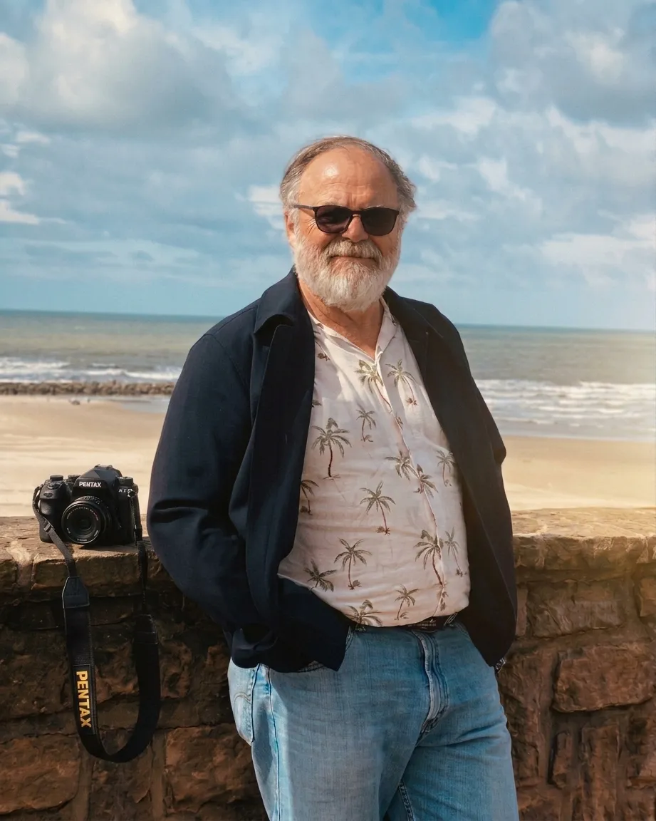 Franck adossé à un muret de pierre au bord de la mer, son appareil photo posé à côté de lui