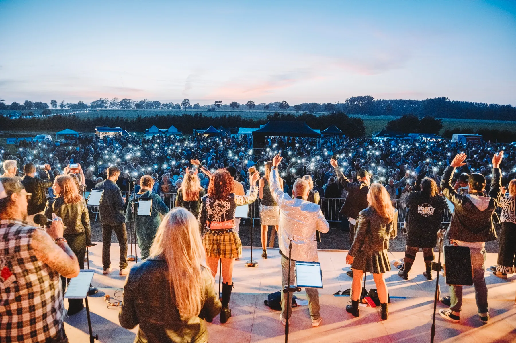 Vue depuis la scène : les artistes face au public illuminé par les téléphones, au crépuscule
